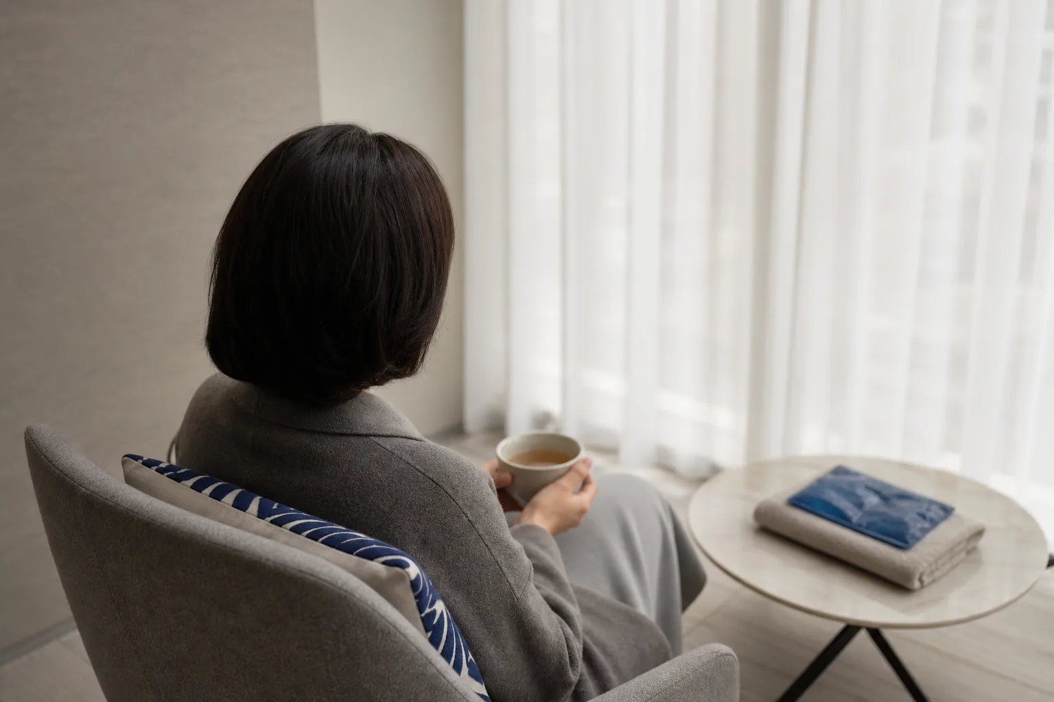 Patient seen from behind resting with a cup of tea in the VOS Dermatology lounge after an injectable session, Gangnam Seoul
