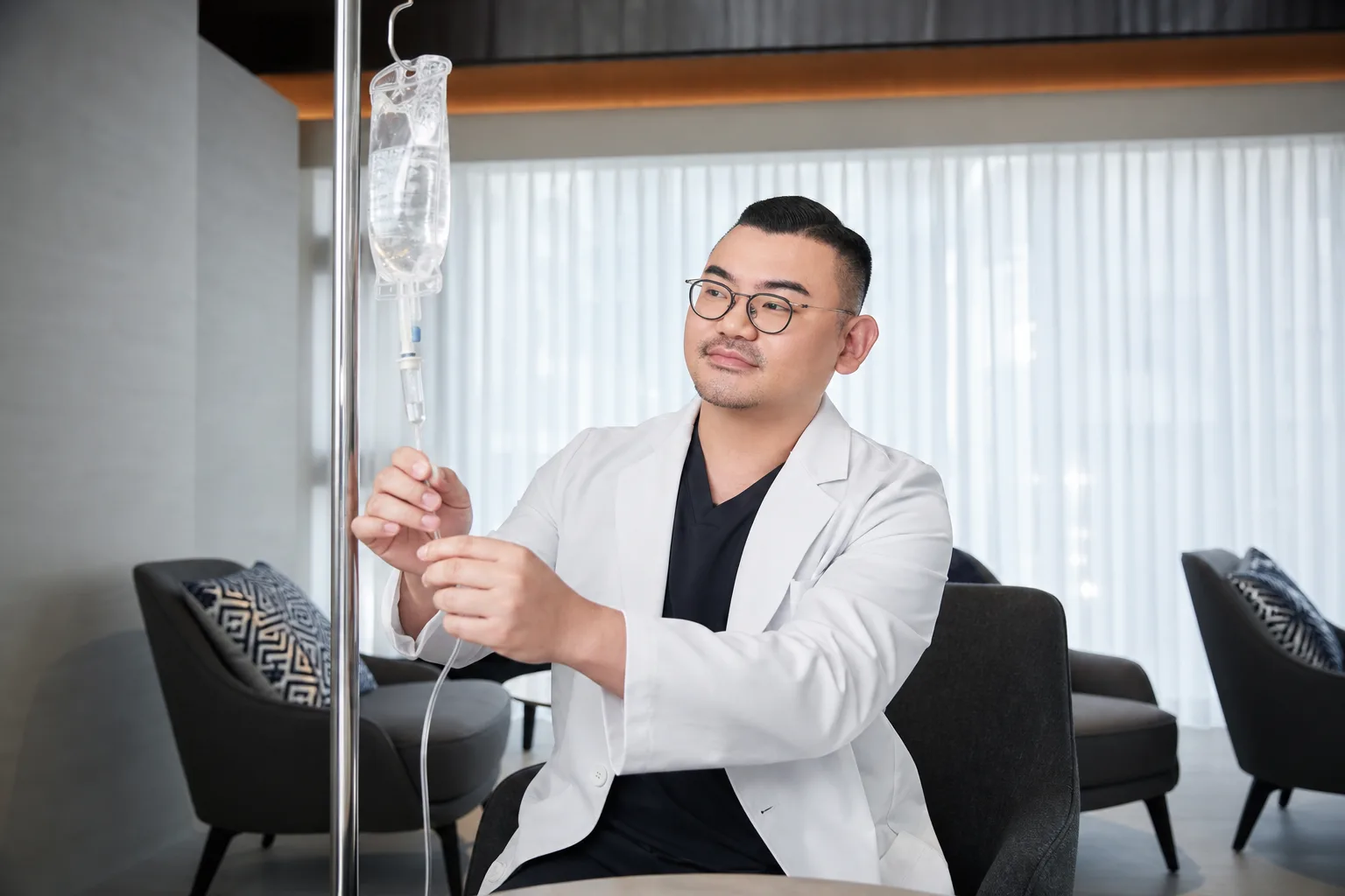 Dr. Hongseok Kim, board-certified dermatologist, examining an IV drip stand in the VOS private lounge, Gangnam