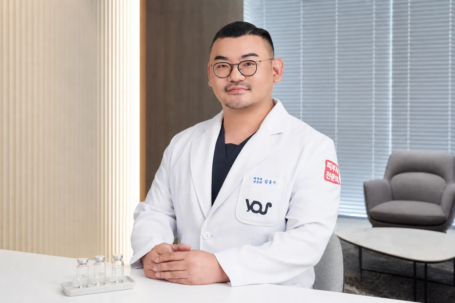 Dr. Hongseok Kim, board-certified dermatologist, seated with skin-booster vials in the VOS consultation room, Gangnam
