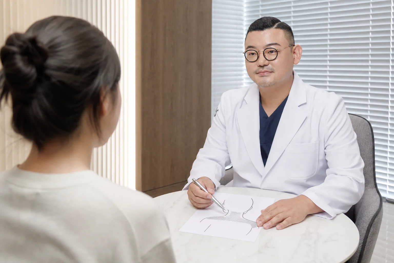 Dr. Hongseok Kim sketching the neck and shoulder line for shoulder slimming injection with a patient seen from behind at VOS Dermatology, Gangnam