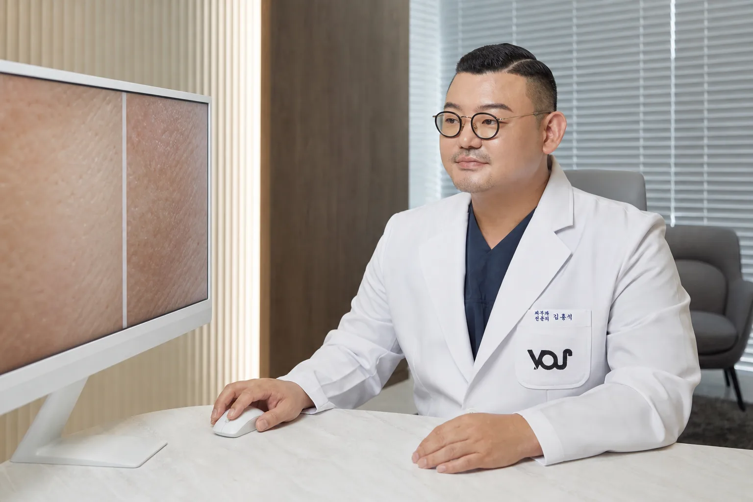 Dr. Hongseok Kim comparing two magnified skin-texture images on a monitor at his desk in VOS Dermatology, Gangnam